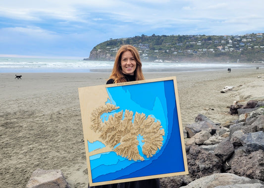 Handcrafted wooden map of Banks Peninsula, New Zealand, showing detailed bathymetry and coastal contours in layered woodcut style
