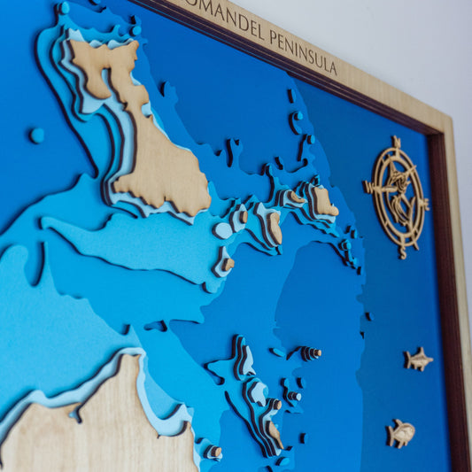 A flat lay of nautical-themed gifts including a custom wooden map, rope keychain, and engraved coordinates keyring—styled on a rustic timber surface with shells and sea charts.