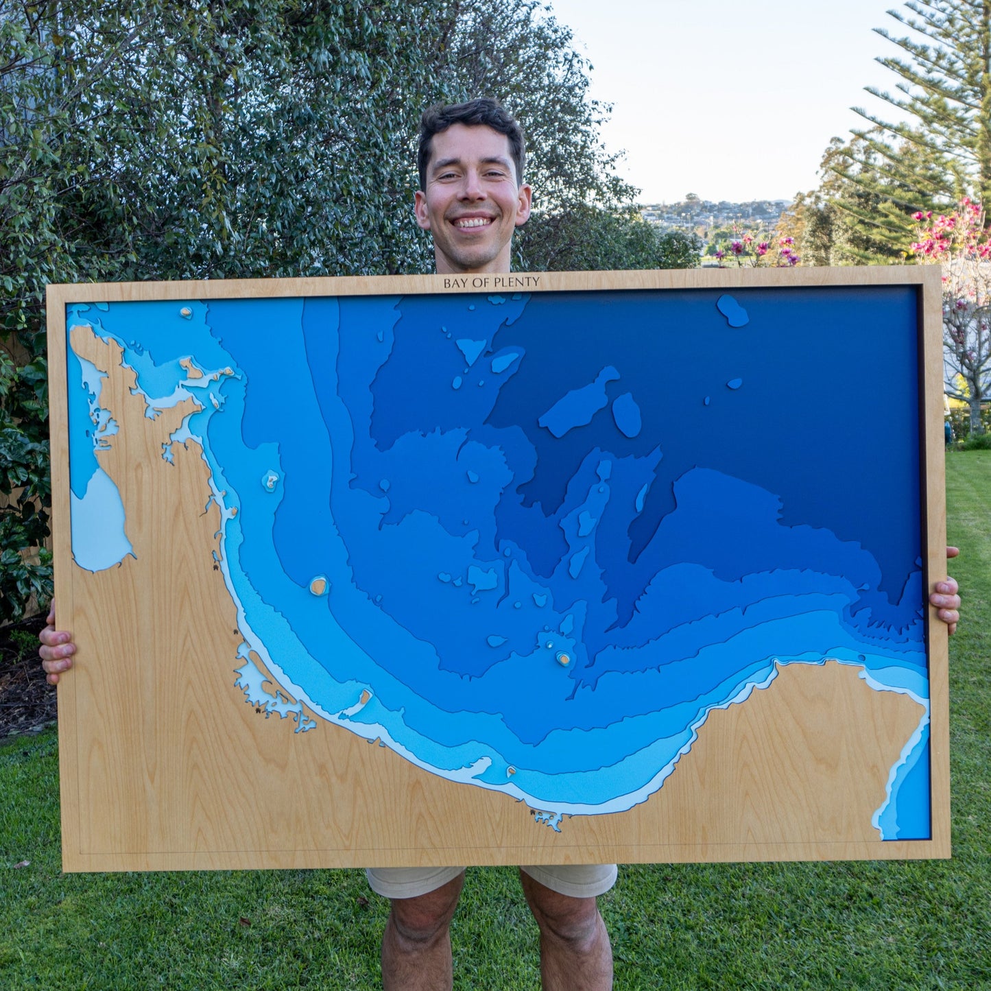 Person holding a large framed topographic map of a coastal area outdoors.