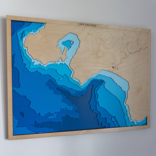 Handcrafted wooden depth map of Cape Palliser, New Zealand, showcasing laser-cut layers depicting the rugged coastline, iconic lighthouse, and surrounding ocean contours.