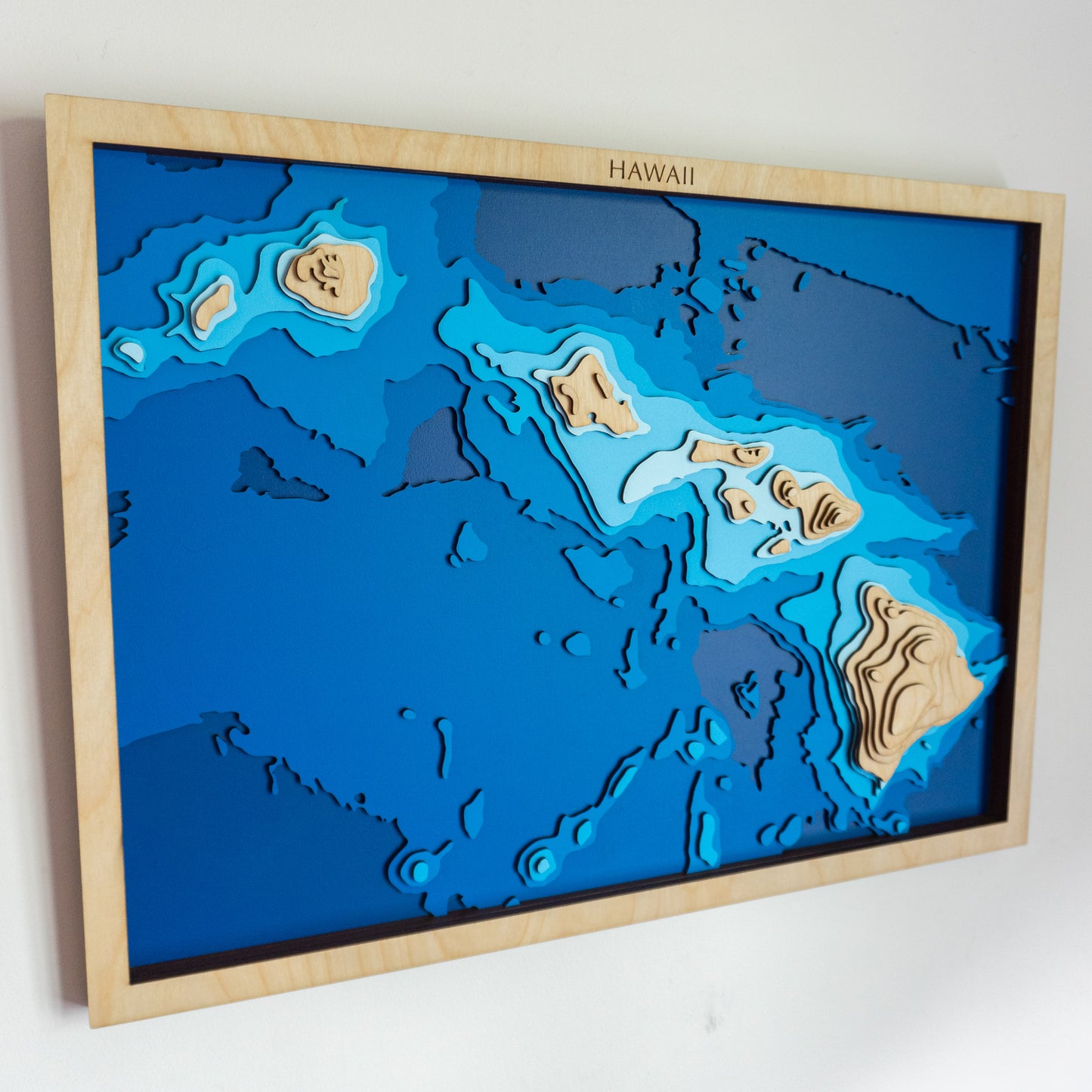 Handcrafted wooden depth map of the Hawaiian Islands, featuring laser-cut European Birch layers illustrating ocean depths from sea level to -5,000 meters, highlighting the archipelago's intricate coastline and surrounding bathymetric contours.