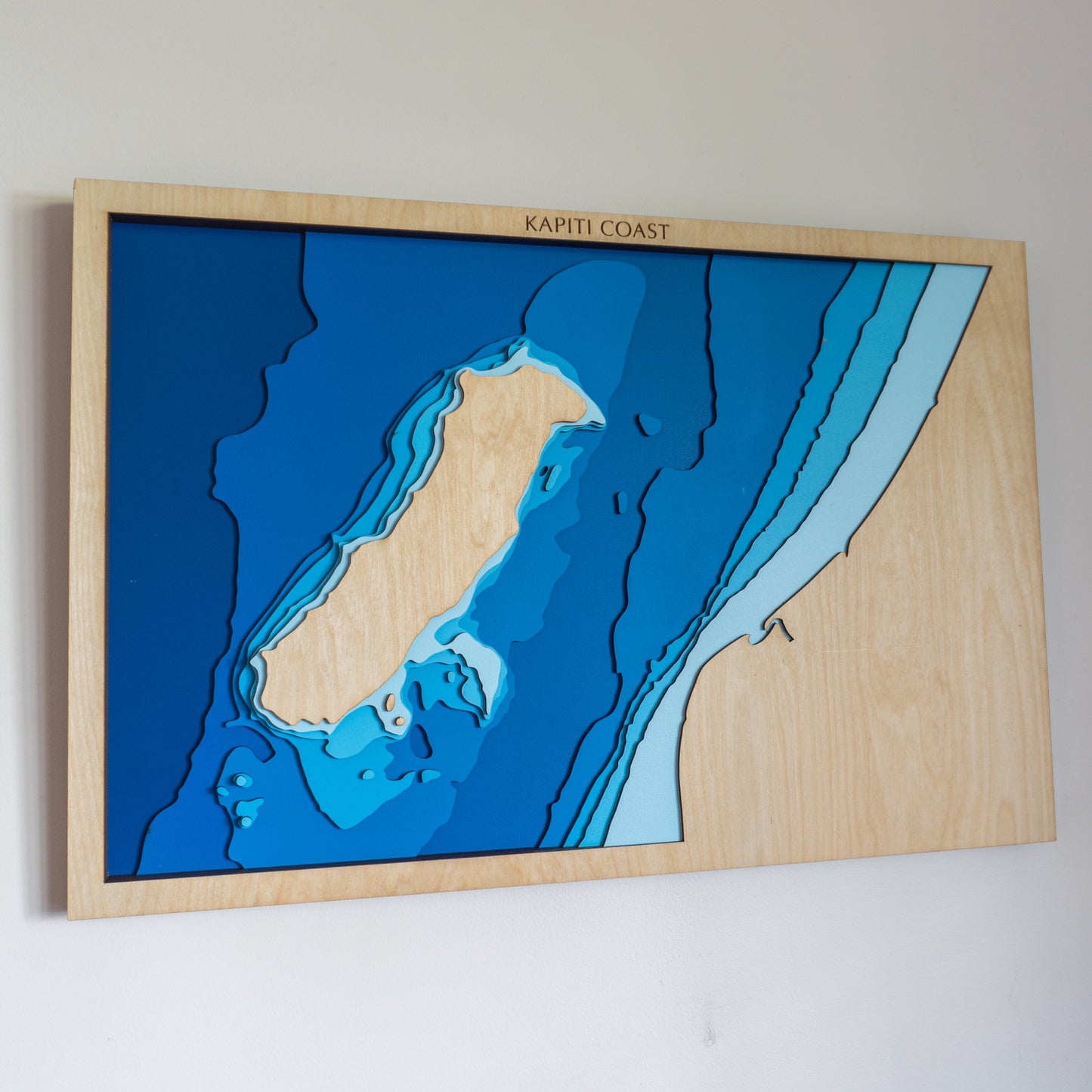 Handcrafted wooden depth map of Kāpiti Island, New Zealand, featuring laser-cut layers illustrating sea depths from sea level to -100 meters.