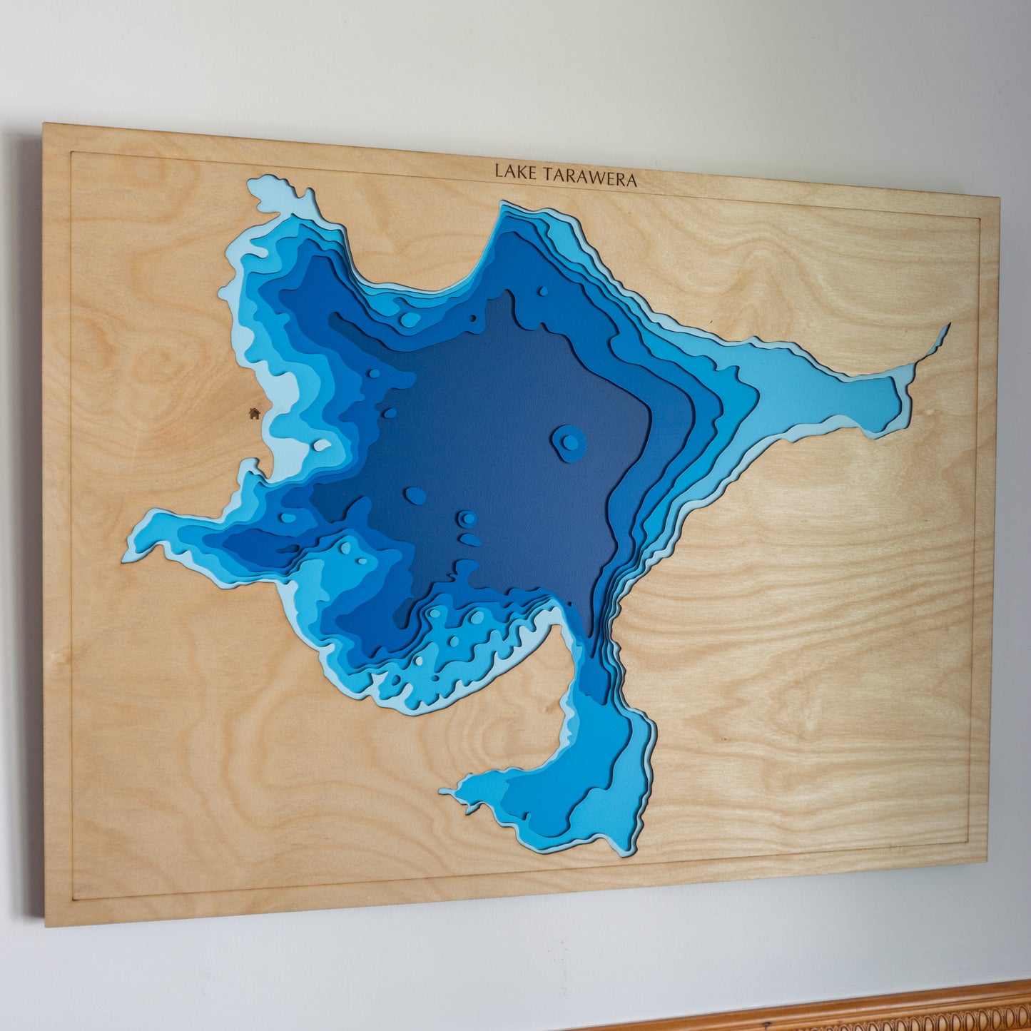 Handcrafted wooden depth map of Lake Tarawera, New Zealand, showcasing laser-cut layers depicting the lake's clear waters, surrounding native forests, and volcanic hills.