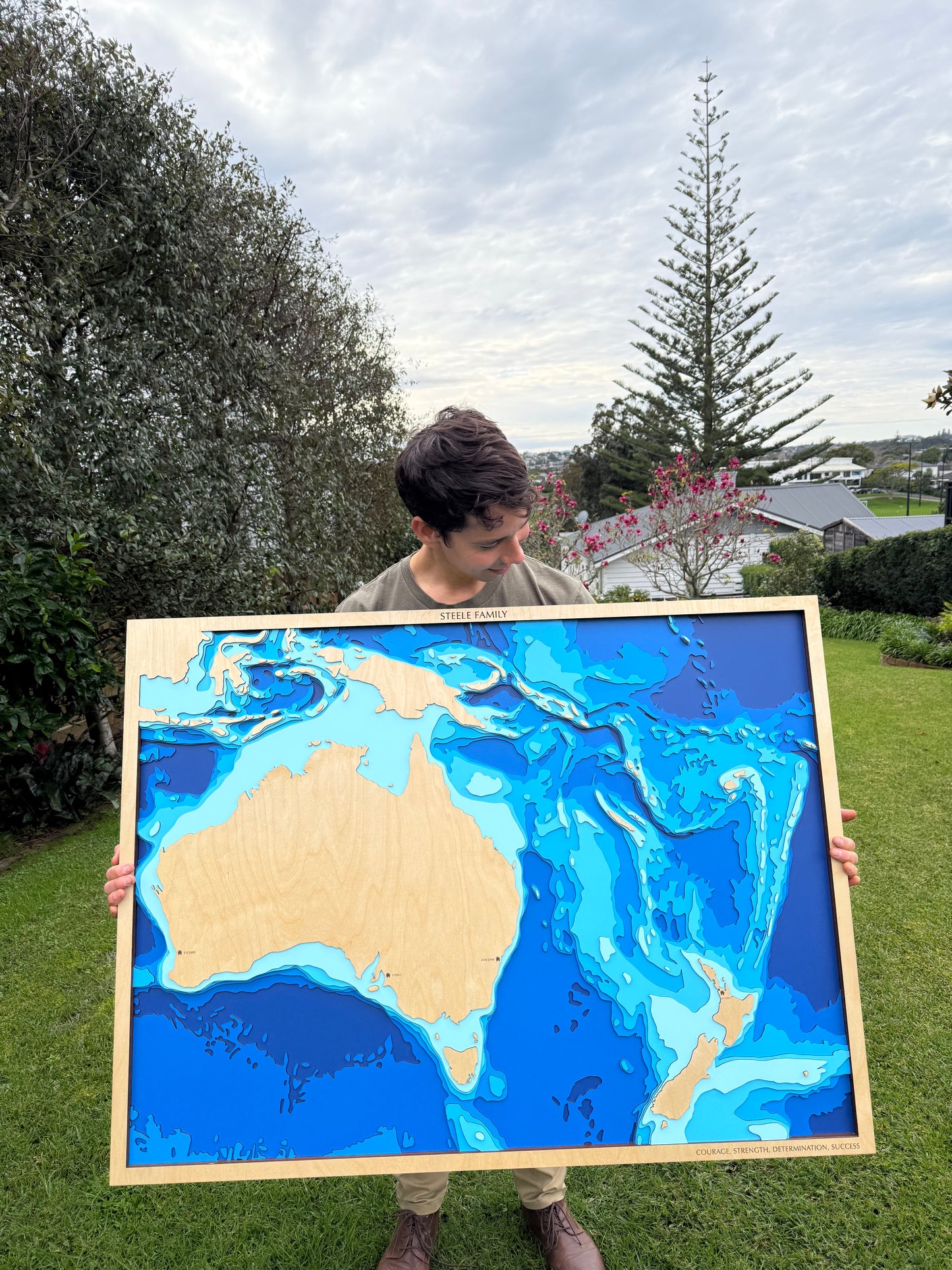 Person holding a large framed topographic map of the world outdoors.