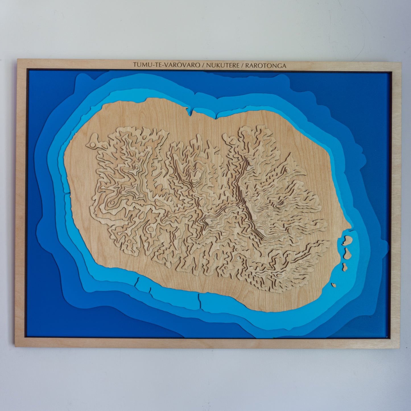 Topographic map of Rarotonga with blue water and brown landmass, framed on a white wall.