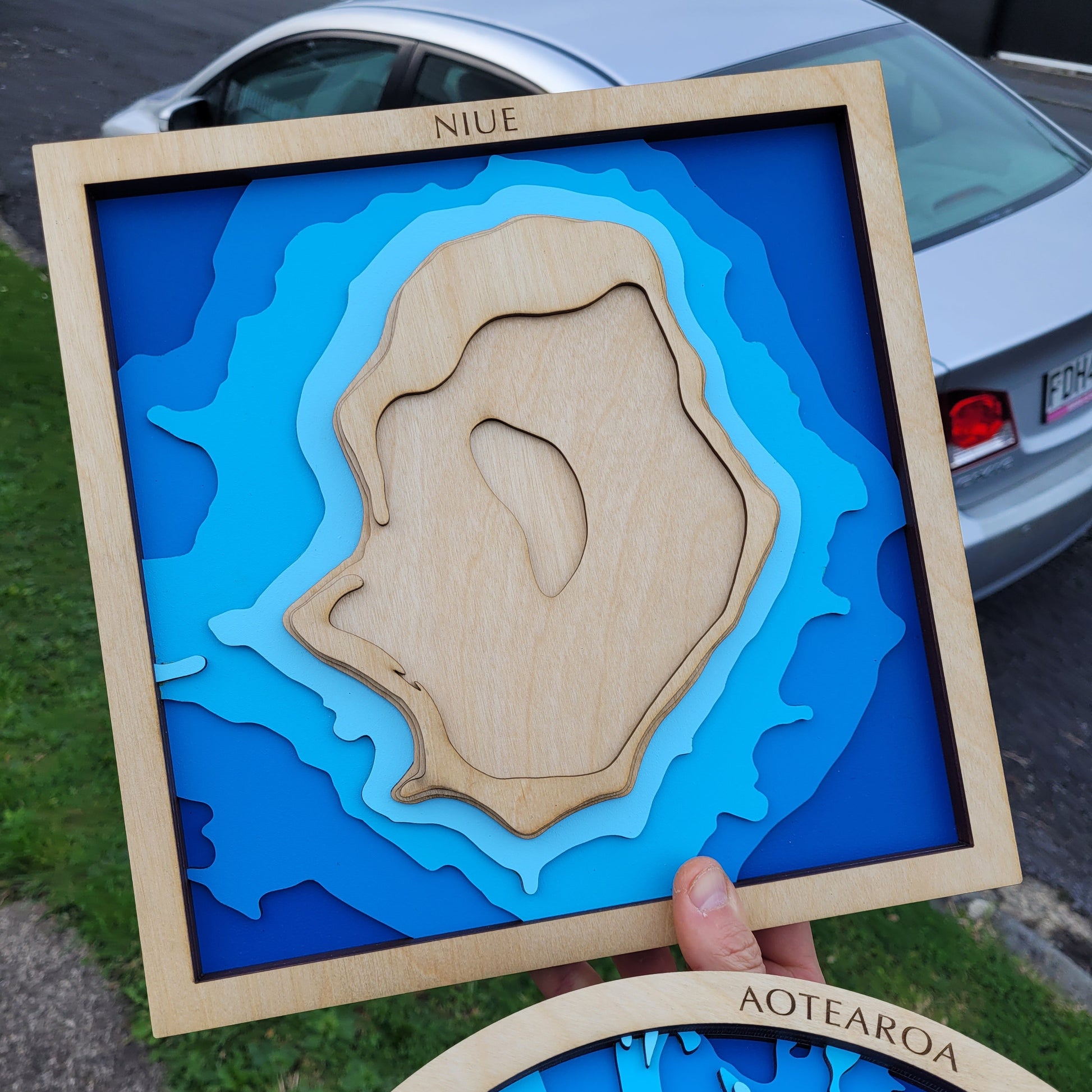 Detailed close-up of the Niue wooden map, showing layered contours, clear edge finishing, and coastal reef textures.