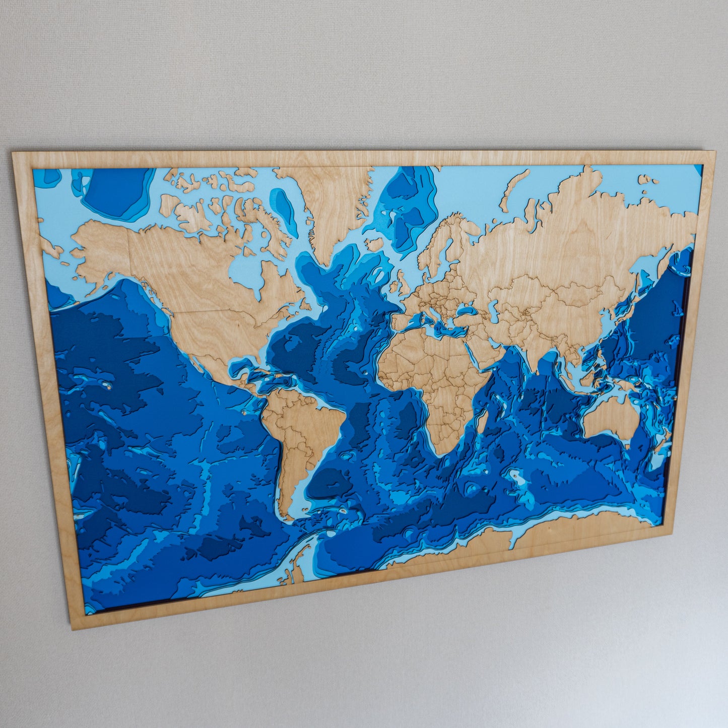 Close-up view of the World XL wooden map showing detailed laser-cut bathymetric layers and global coastal features.