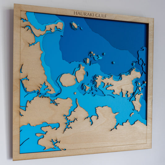 Handcrafted wooden depth map of the Hauraki Gulf, New Zealand, featuring laser-cut layers depicting sea depths from sea level to -50 meters, highlighting coastal contours and islands.