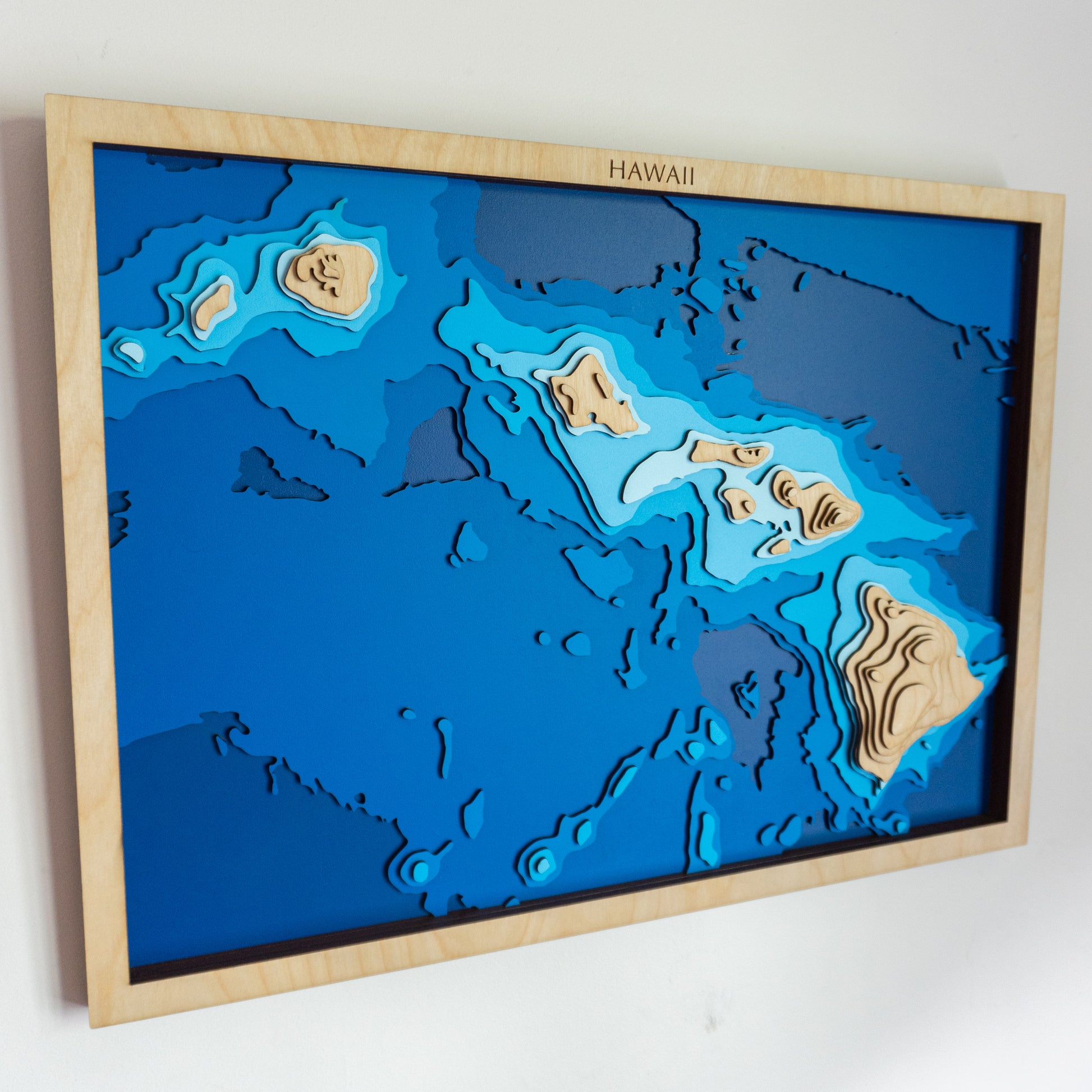 Handcrafted wooden depth map of the Hawaiian Islands, featuring laser-cut European Birch layers illustrating ocean depths from sea level to -5,000 meters, highlighting the archipelago's intricate coastline and surrounding bathymetric contours.