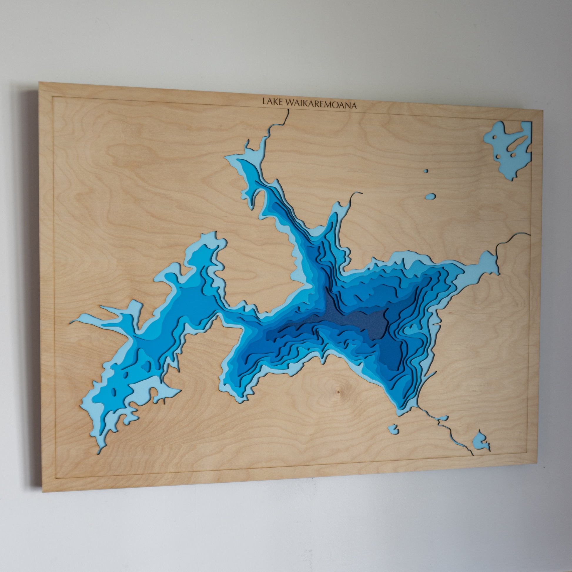 Handcrafted wooden depth map of Lake Waikaremoana, showcasing laser-cut layers depicting the lake's clear waters, surrounding dense forests, and rolling hills.