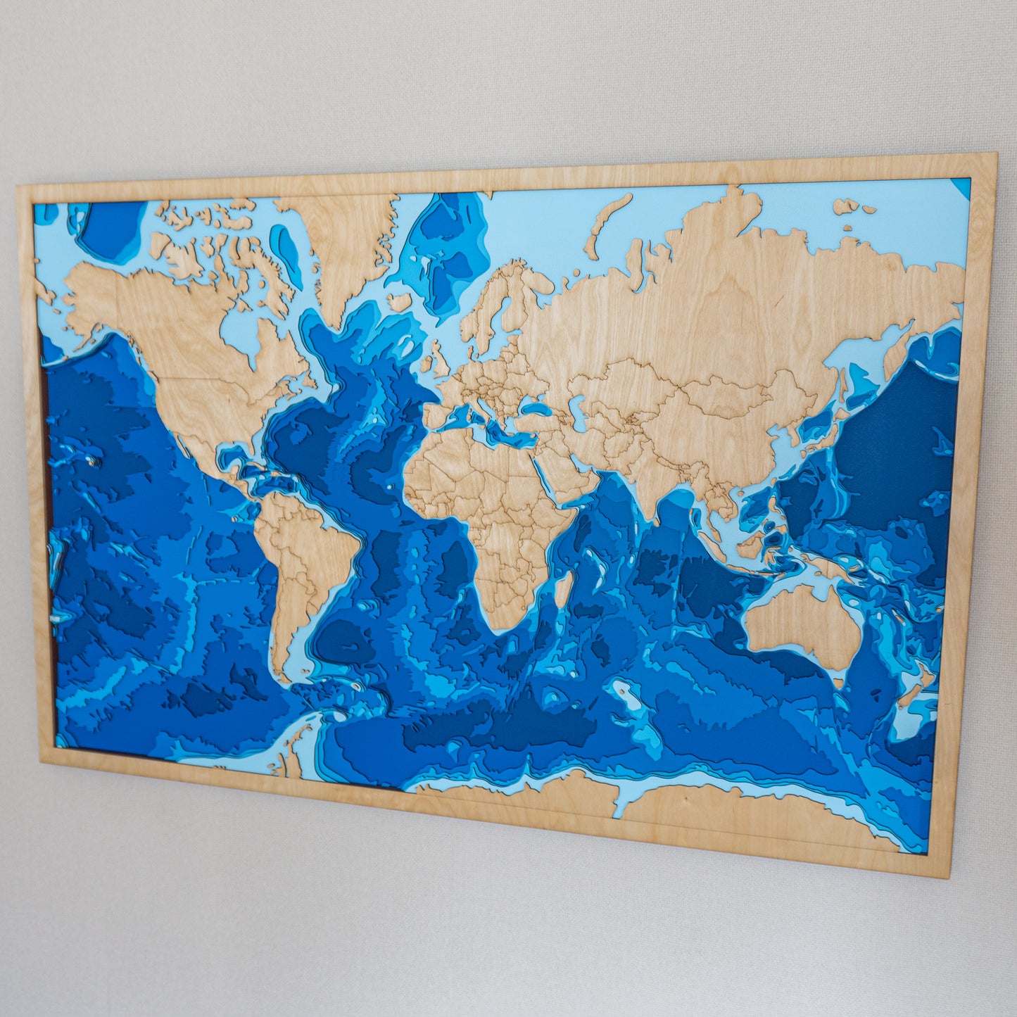 Extra-large handcrafted wooden depth map of the world, featuring laser-cut birch layers illustrating ocean depths from sea level to -6,000 meters, highlighting global coastlines and bathymetric contours.